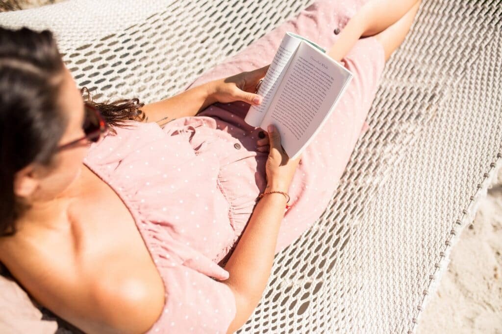 Girl in pink dress reading travel books in a hammock